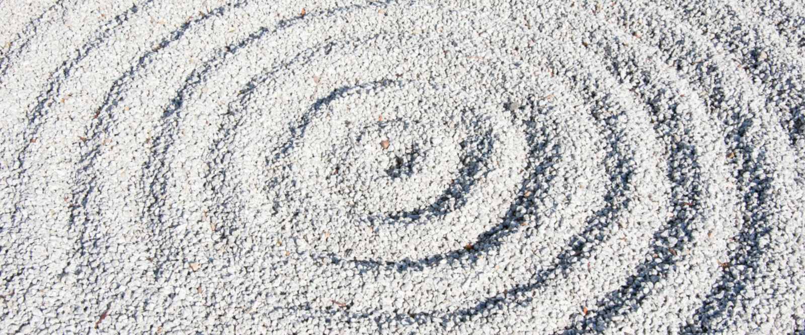 Raked gravel in a dry garden, drawn into concentric rings around a still centre.